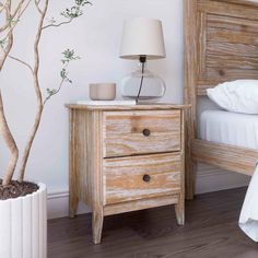 a white bed sitting next to a wooden night stand with a lamp on top of it