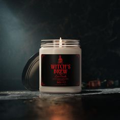 a white candle sitting on top of a wooden table next to a black container with a red label that says witch's brew