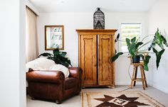 a living room filled with furniture and a tall wooden cabinet next to a plant on top of a rug