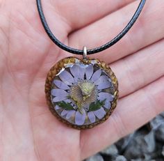 a hand holding a small purple flower in it's center with green leaves on top