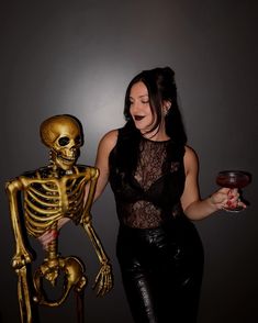 a woman standing next to a skeleton holding a drink