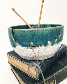 two books are stacked on top of each other and one is holding a bowl with wooden spoons in it