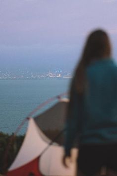 a woman is standing in front of an umbrella looking out at the ocean and buildings