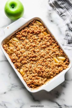 a casserole dish filled with apples and crumbled topping on a marble surface