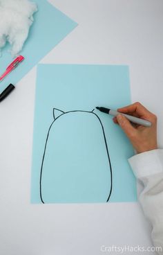 someone is drawing a cat on a piece of paper with a marker and some clouds in the background