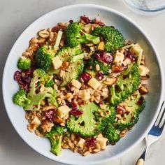 a white bowl filled with broccoli, nuts and cranberry salad next to a fork