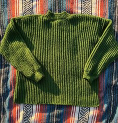 a green sweater sitting on top of a colorful blanket