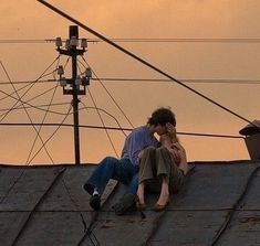 two people sitting on the roof of a building talking on their cell phones at sunset