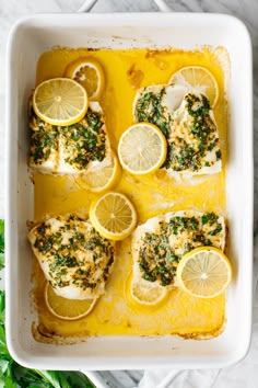 baked fish with lemons and herbs in a white casserole dish on a marble table