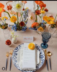 the table is set with blue and white plates, silverware, and colorful flowers