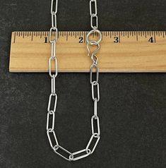 a long silver chain with a measuring tape on the side and a wooden ruler behind it