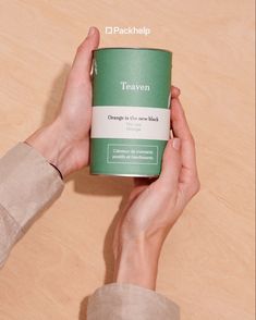 a person holding a can of tea on top of a wooden table