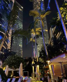 an outdoor swimming pool surrounded by palm trees and skyscrapers at night in the city