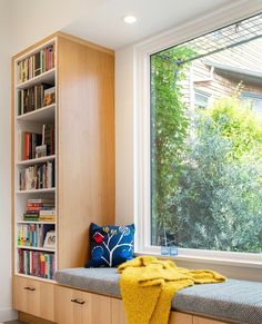 a window seat with a yellow blanket on it in front of a bookshelf