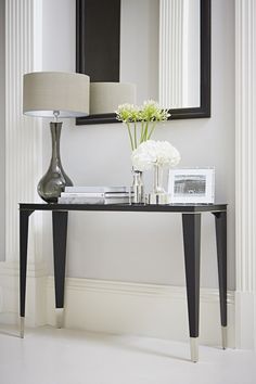 a black table with flowers and pictures on it in front of a large mirror, lamp and framed photograph