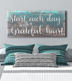 a bed with pillows and a wooden sign above it that says start each day with a grateful heart