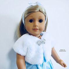 a doll with blonde hair wearing a blue dress and white fur stoler, standing against a wall