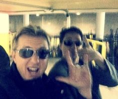 two men taking pictures with their cell phones in a parking garage while one man holds his hand up to the camera