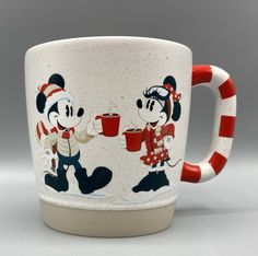 mickey and minnie mouse coffee mugs with candy cane handles are shown in front of a gray background