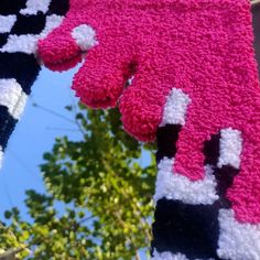 two knitted mitts hanging from a clothes line with trees in the background and blue sky