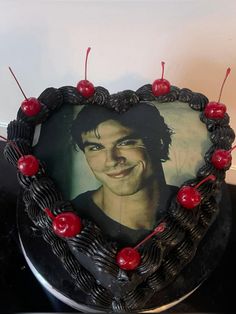 a black heart shaped cake with cherries around it and a photo of the actor