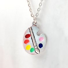 "This colorful painter's necklace is made with an antiqued silver paint palette pendant which we hand-enameled with rainbow colors and, of course, a little pink. The paint palette charm hangs on an 18-inch rhodium cable chain and makes a great gift for artists, watercolor or oil painters, art teachers or any creative person. Thank you for looking. NOTE: This listing is for one necklace with one pendant, but you can choose to purchase just the pendant without the chain (see drop down menu). The \ Artistic Multicolor Nickel Free Necklace, Artistic Multicolor Nickel-free Necklace, Artsy Nickel-free Pendant Necklace, Artsy Silver Pendant Necklace, Artsy Adjustable Silver Necklace, Adjustable Silver Artsy Necklace, Adjustable Silver Artsy Necklaces, Adjustable Multicolor Enamel Necklace, Adjustable Artsy Silver Necklace