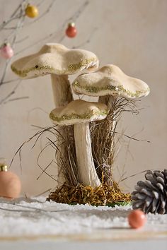 three white mushrooms sitting on top of snow covered ground next to pine cones and ornaments