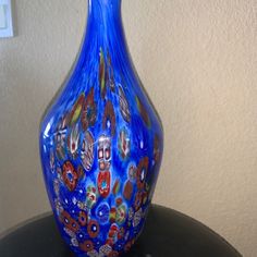 a blue glass vase sitting on top of a black table next to a white wall