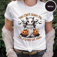 Show off your fun side this Halloween season with this charming "You Can't Scare Me, I'm a Crazy Cat Mom" t-shirt designed for cat lovers with a twist of Halloween spirit, this shirt features a captivating graphic of a cat dressed in a ghostly costume, surrounded by pumpkins and playful bats. Made from 100% cotton, the Bella Canvas 3001 shirt offers both comfort and durability, making it ideal for everyday wear. It comes in a classic white color, providing a perfect backdrop for the vivid, spooky-themed graphic. Lightweight, with just the right amount of stretch, it's flattering for all body types. This shirt is not only a great addition to your own wardrobe but also makes a wonderful gift for any cat enthusiast in your life who embraces their quirky side. Whether you're attending a Hallow White Cat Print T-shirt For Halloween, White T-shirt With Cat Print For Fall, Halloween White T-shirt With Cat Print, Halloween Graphic Tee With Cat Design, Halloween Cat Print Graphic Tee, Halloween Cat Design Graphic Tee, White Cat Print T-shirt For Fall, White T-shirt With Cat Design For Fall, Spooky Halloween T-shirt With Cat Design