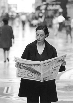 a woman reading a newspaper while walking down the street