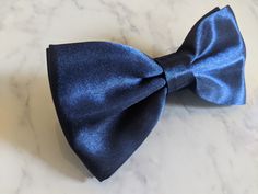 Upgrade your wardrobe in style with this stunning blue satin bow tie. Perfect gift for him, this unique adjustable bow tie will elevate your style for any occasion including weddings, birthdays and anniversaries. Comes pre-tied. Elegant Blue Bow For Wedding, Elegant Blue Party Ties, Formal Blue Suit And Bow Tie Accessories, Elegant Blue Bow Tie, Formal Blue Bow Tie And Suit Accessories, Blue Satin Bow Tie For Weddings, Blue Tie With Bow Tie Back As A Gift, Classic Blue Ties For Party, Blue Bow With Bow Tie Back For Wedding