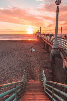 the sun is setting at the beach with stairs leading to the water