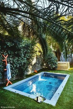 a person standing in front of a pool surrounded by grass and palm trees, reaching up into the air