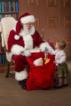 a little boy standing next to santa clause sitting in a chair with his legs crossed