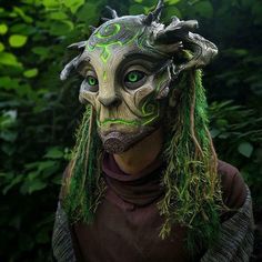 a man with green hair wearing a mask and dreadlocks in front of trees