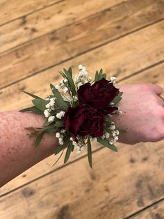 a woman's arm with flowers and greenery attached to it on top of a wooden floor