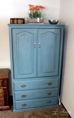 a blue armoire with two drawers and a potted plant on top