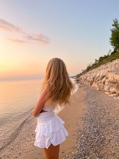 a woman standing on top of a sandy beach next to the ocean with her back to the camera