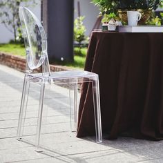 a clear chair sitting on top of a sidewalk next to a potted plant