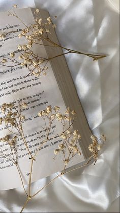 an open book sitting on top of a bed covered in white sheets and dried flowers