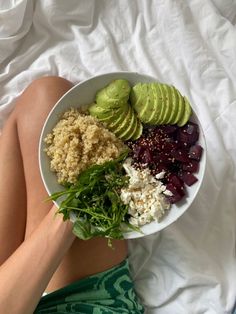 a woman laying on her side holding a bowl of food with avocado, beets and rice