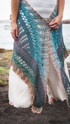 a woman is standing on the beach wearing a crocheted shawl