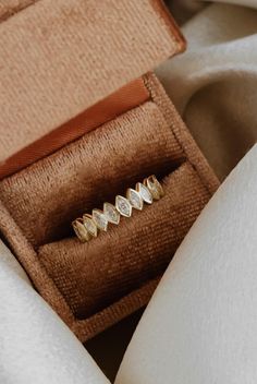 a gold ring with five diamonds in it sitting inside an open box on top of a white cloth