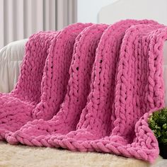 a pink crocheted blanket sitting on top of a bed next to a potted plant