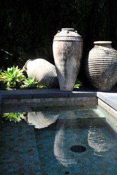 two large vases sitting on top of a swimming pool next to plants and trees