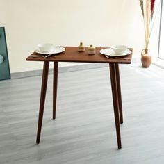 a wooden table with two plates on it in front of a vase and potted plant