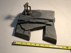 a piece of rock with a small statue on it next to a measuring tape and a hammer