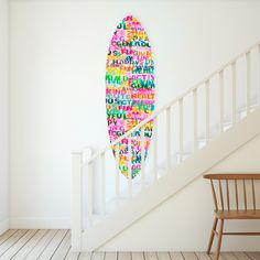 a colorful surfboard is hanging on the wall next to a stair case in a white room