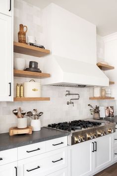 a kitchen with white cabinets and stainless steel stove top oven, open shelving above the range