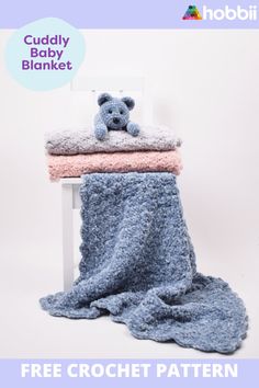 a crocheted teddy bear laying on top of a blanket next to a white chair